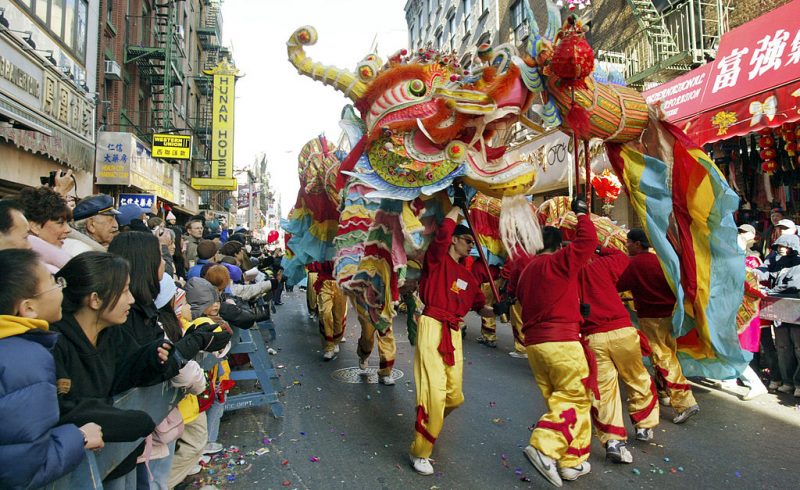 Lunar New Year: People in red and yellow carry a dragon float over their heads through a street lined with festive onlookers.