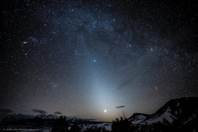 Night sky with snow covered mountains in the foreground.