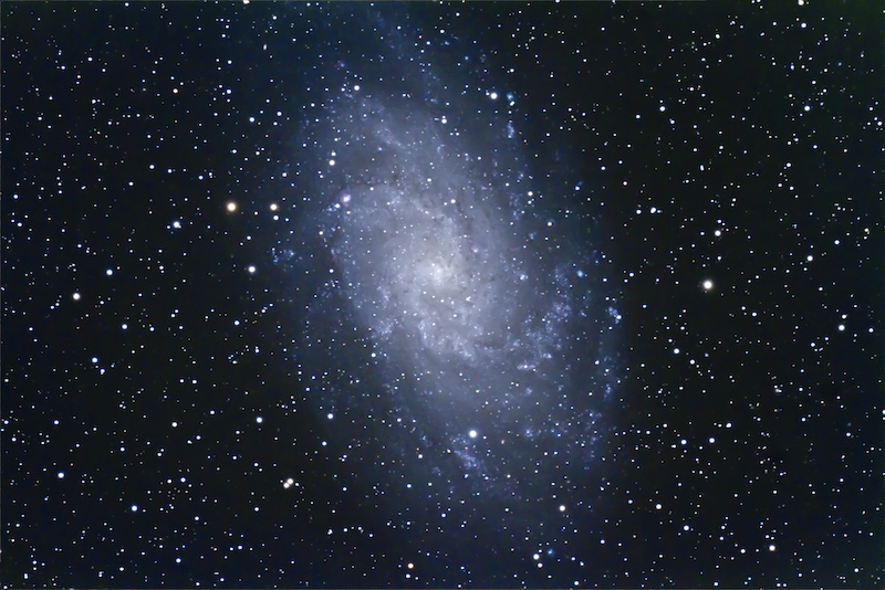 A nebulous white pinwheel-shaped spiral galaxy with very many stars in the foreground.