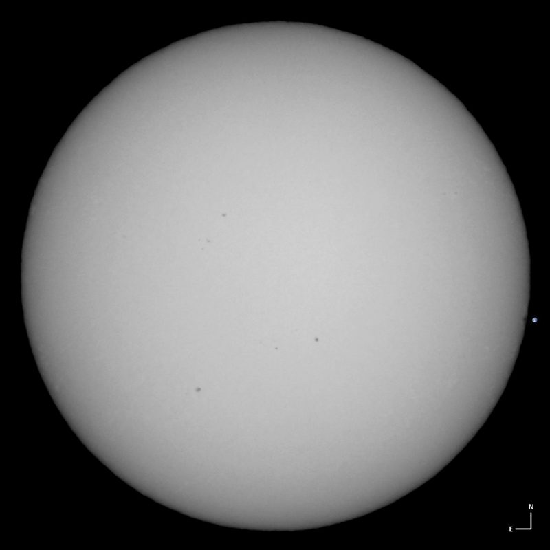 The sun, seen as a large white sphere with small dark spots.