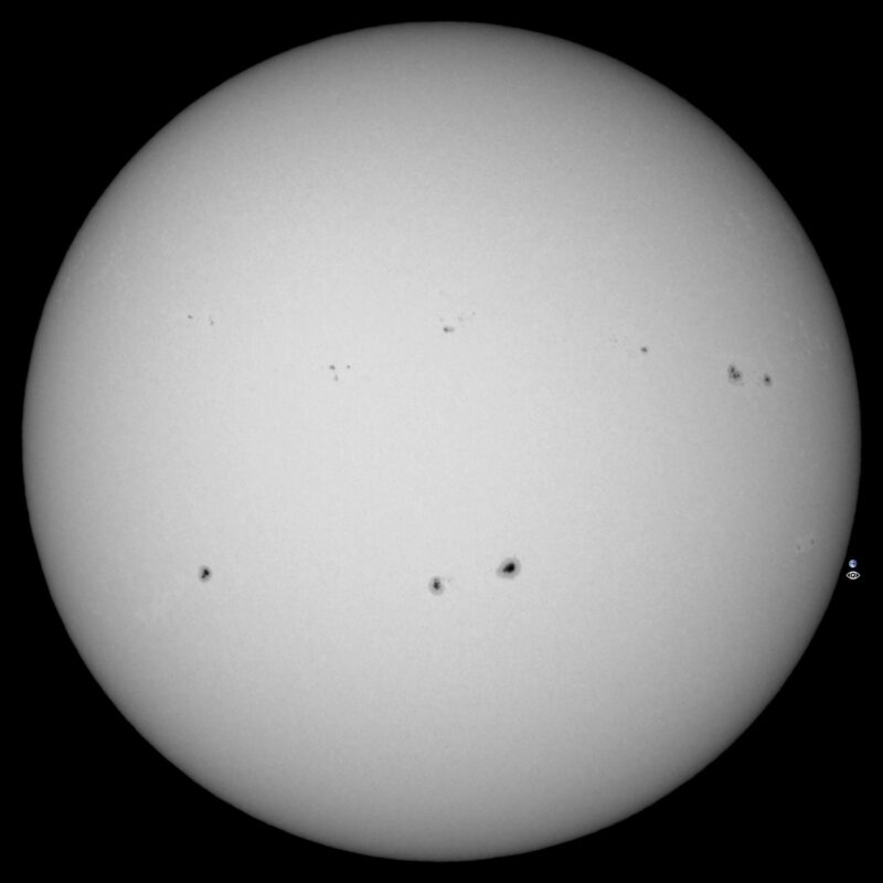 The sun, seen as a large white sphere with small dark spots.