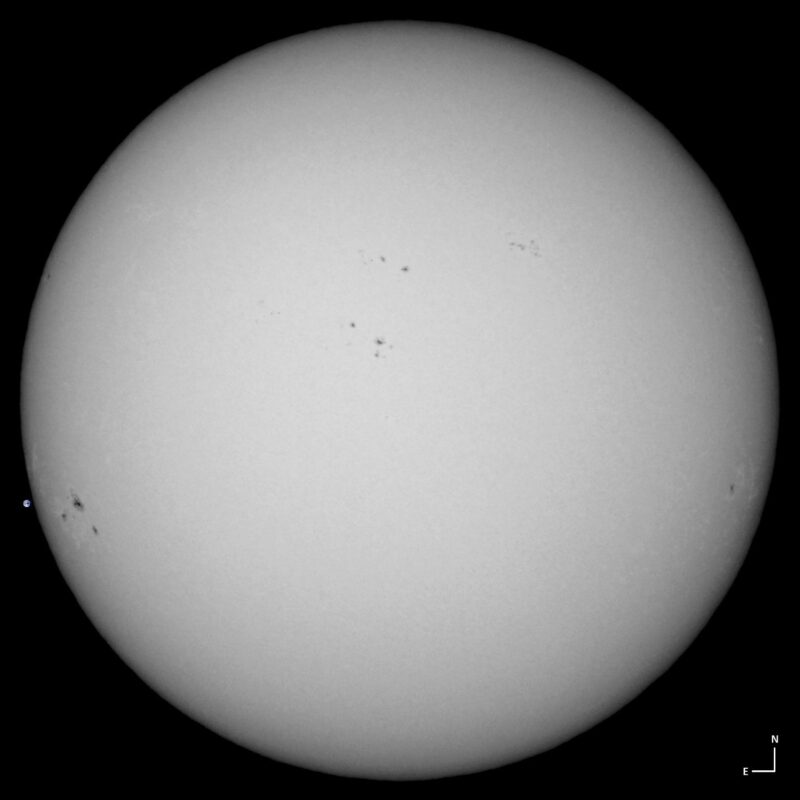 The sun, seen as a large white sphere with small dark spots.