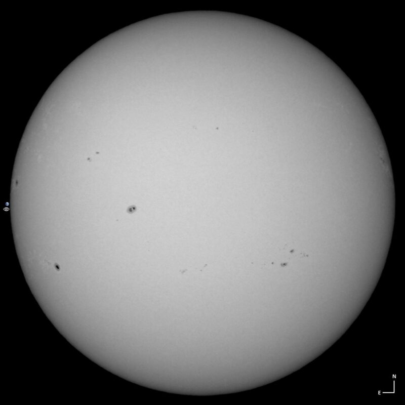 The sun, seen as a large white sphere with small dark spots.