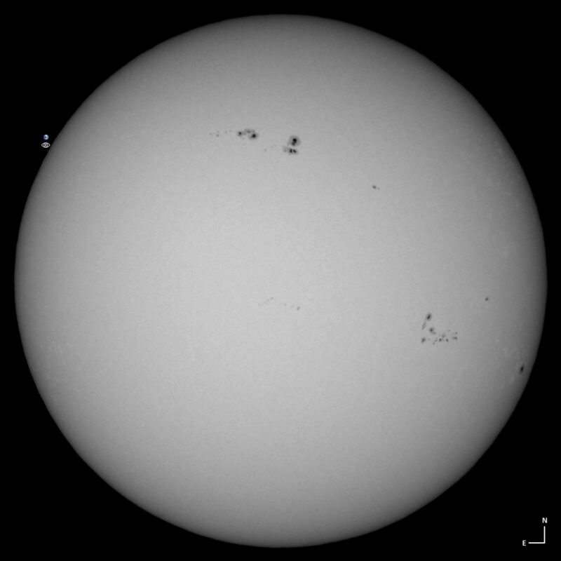 The sun, seen as a large white sphere with small dark spots.