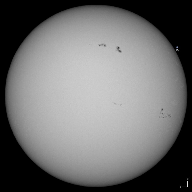 The sun, seen as a large white sphere with small dark spots.