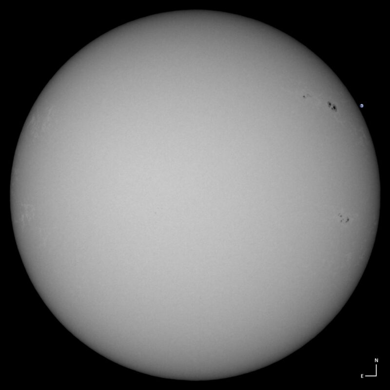 The sun, seen as a large white sphere with small dark spots.