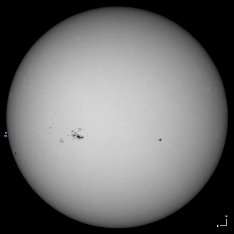 The sun, seen as a large white sphere with small dark spots.