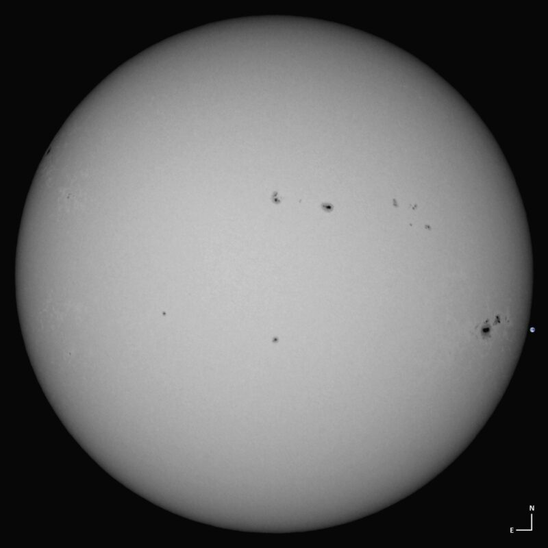 The sun, seen as a large white sphere with small dark spots.