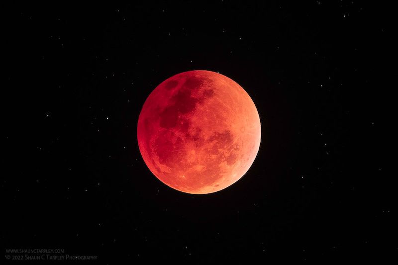 Red full moon on a black background with a few faint stars.