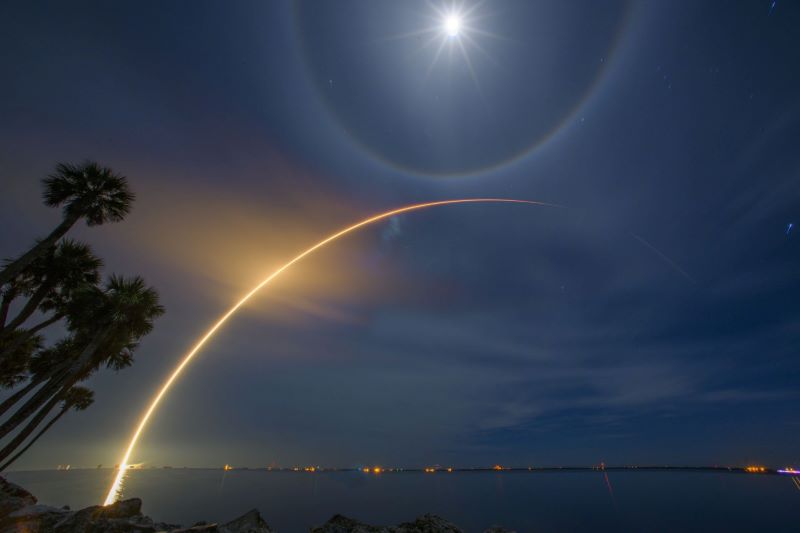 Starlink: Night on the beach with a bright moon overhead and a streak of orange making an arc upward.