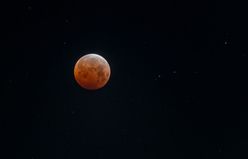 Total lLunar eclipse: Shining orange moon with streak of white on top on a black sky background.