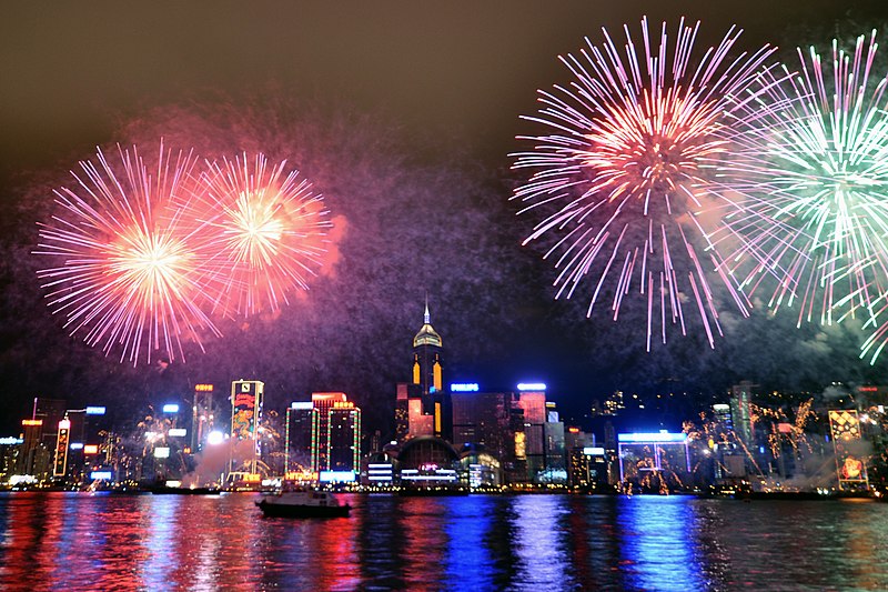 Lunar New Year: Fireworks over a glittering nighttime city skyline with water in the foreground.